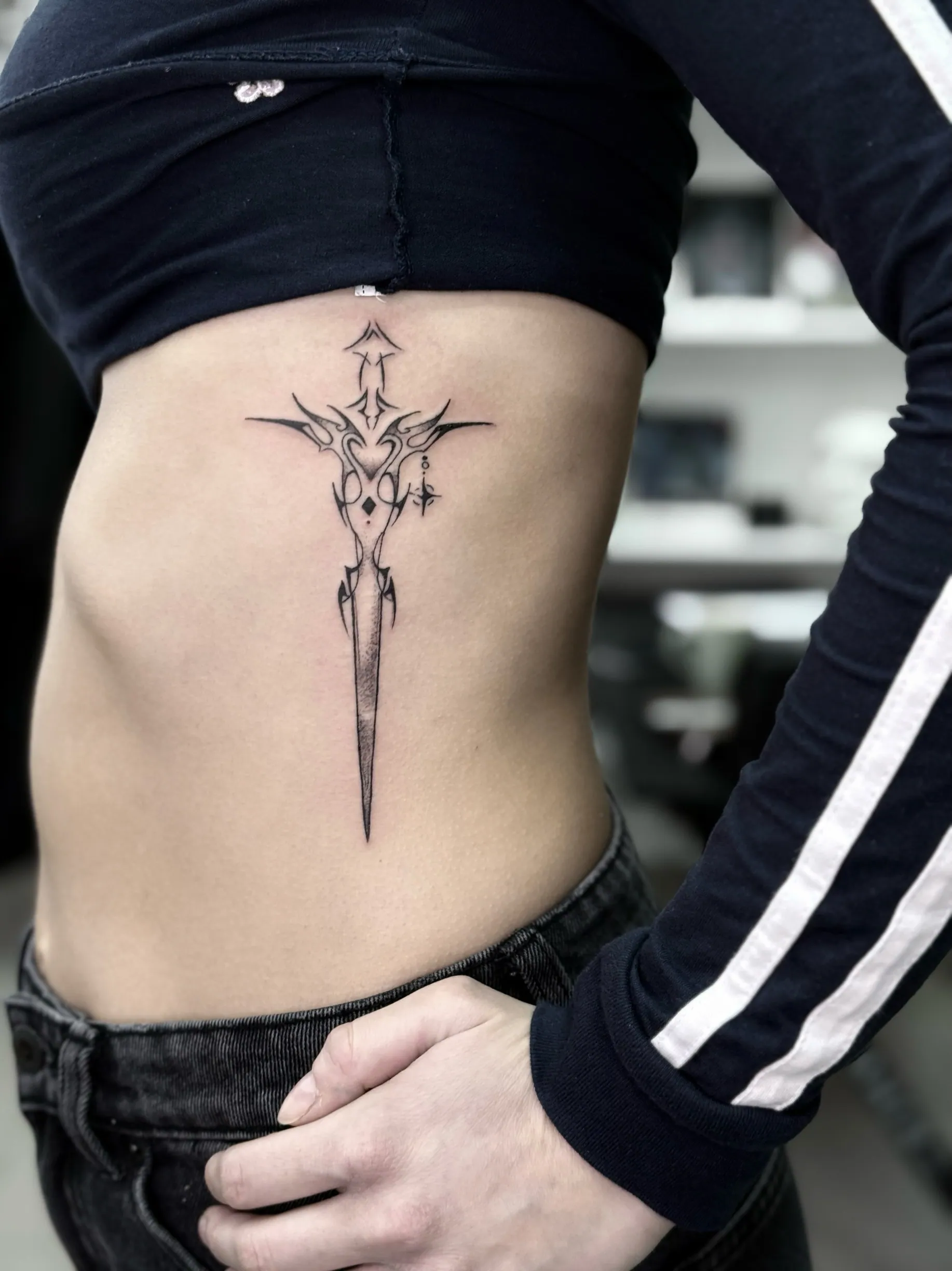 Fine line tetovaža ornamentalnog bodeža sa tribal elementima na rebrima, Dropz Tattoo Studio Niš