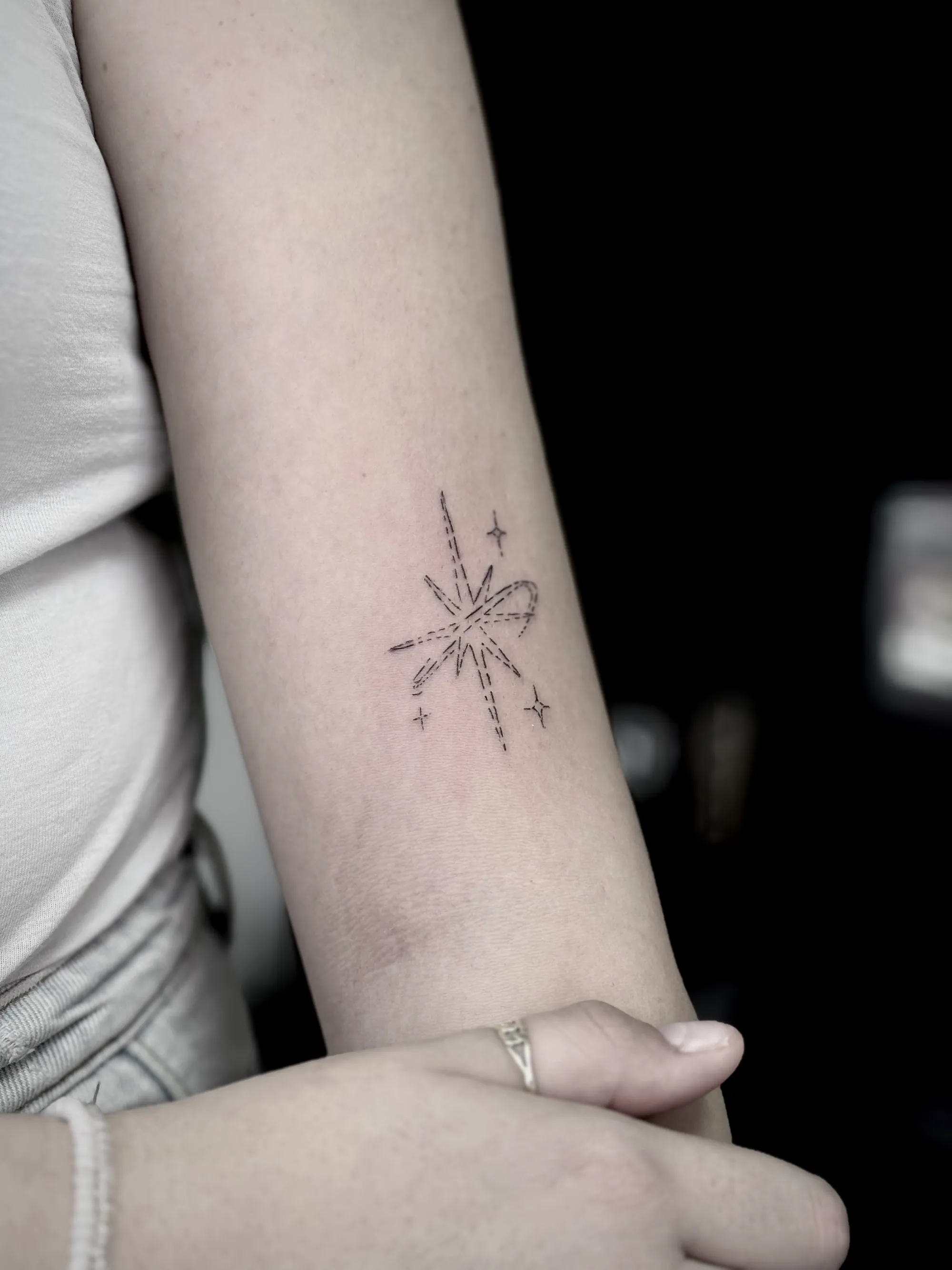 Fine line minimalistička tetovaža zvezde eksplozije sa mašnicom na podlaktici, Dropz Tattoo Studio Niš